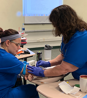 Two medical assisting course students participate in a blood drawing activity